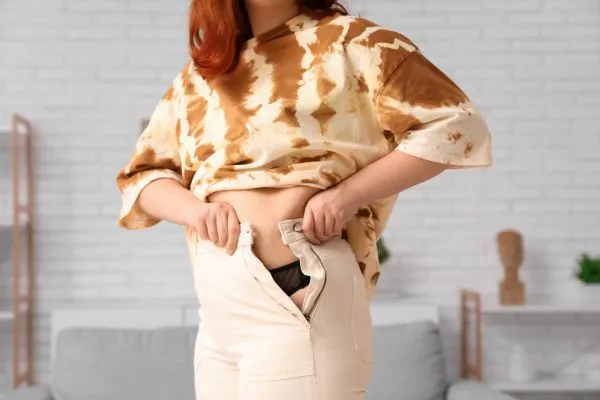 Image of woman trying to do her trousers up after pregnancy weight gain Portsmouth